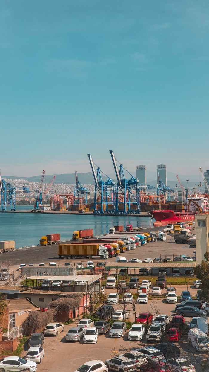 A busy day at the İzmir harbor showcasing cargo ships, cranes, and vehicles in an urban setting.