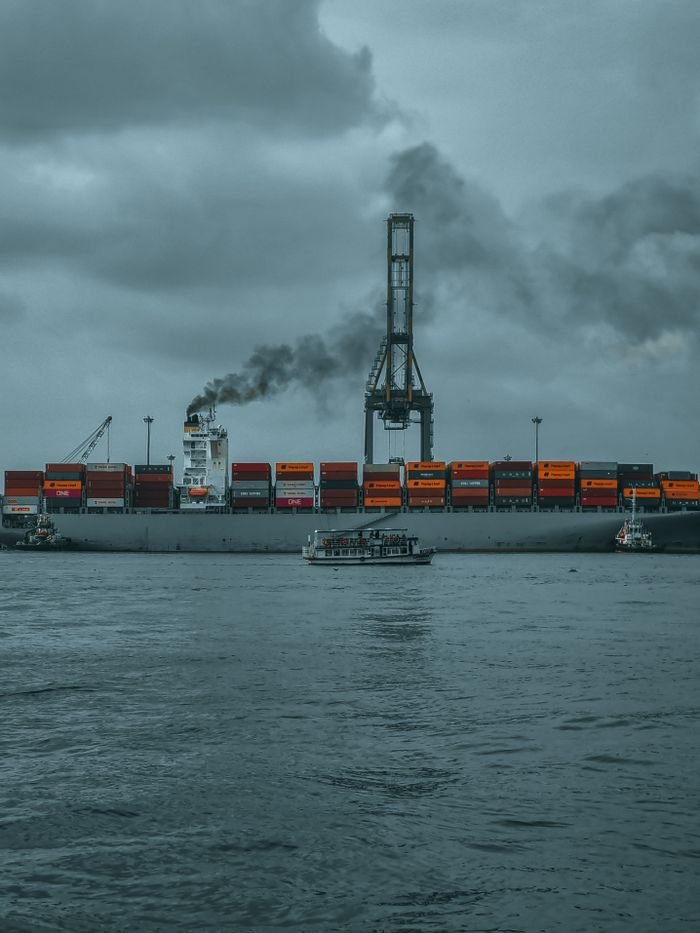 A cargo ship emitting smoke in Kochi harbor under moody skies, showcasing industrial maritime transport.