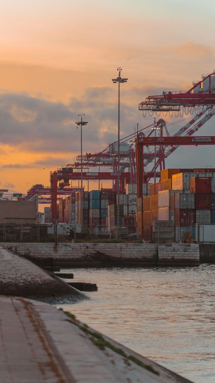 Colorful shipping containers and cranes at a port during sunset.