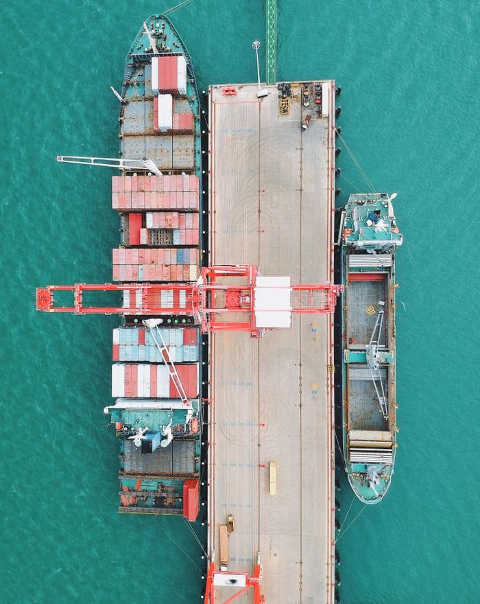 Aerial shot of cargo ships docked at a harbor with cranes and containers.